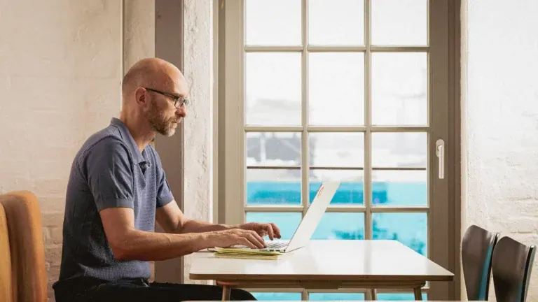 Adobe-Mitarbeiter Jens Heisterkamp arbeitet konzentriert am Laptop an einem Tisch vor einem großen Sprossenfenster mit Hafenblick, fotografiert von Frank Erpinar
