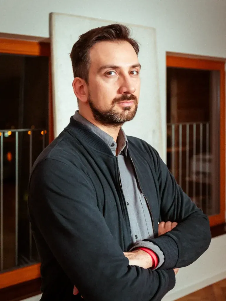 Portrait des Fotografen Dom Quichotte mit verschränkten Armen in dunkler Jacke vor einem Fenster, fotografiert von Frank Erpinar