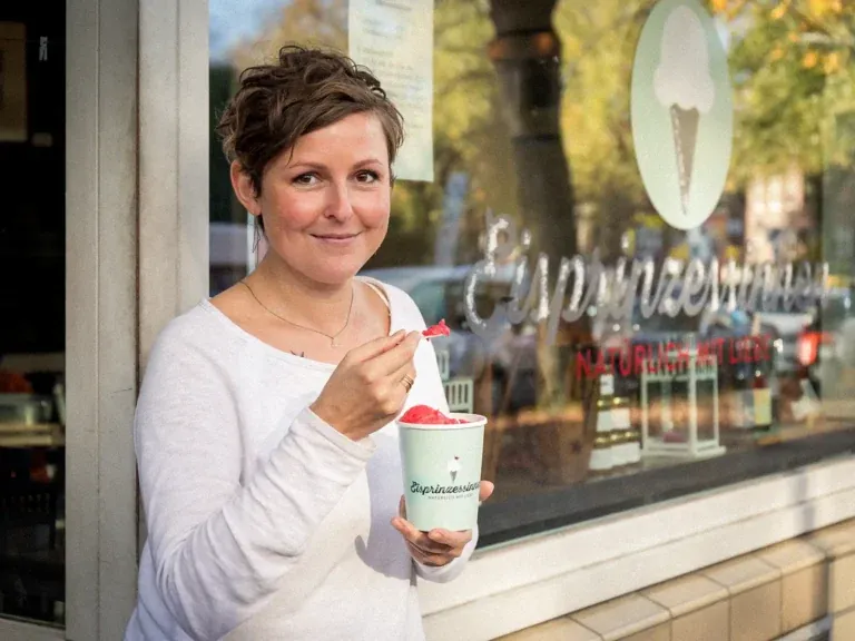 Katrin Kerkhoff hält lächelnd einen Eisbecher vor ihrer Hamburger Eisdiele „Eisprinzessinnen"