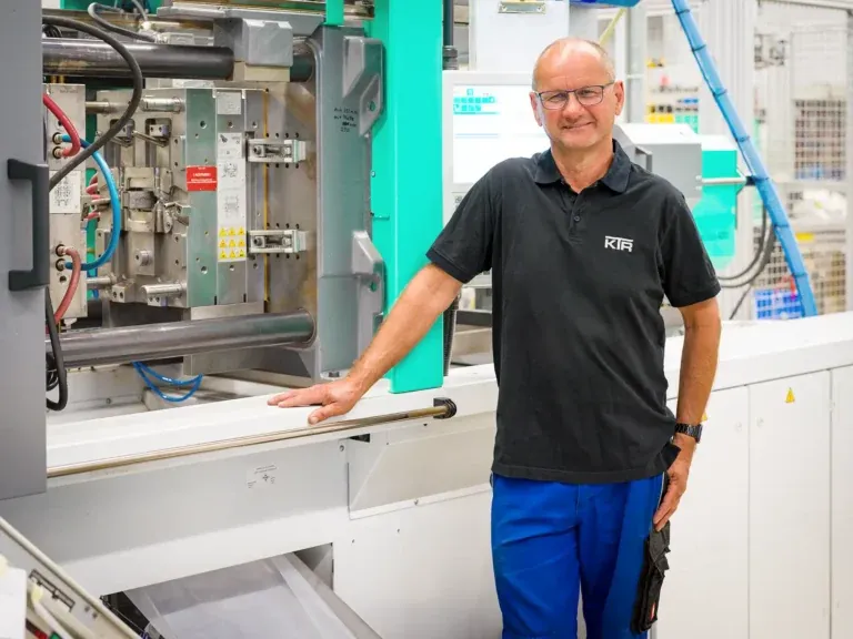 Portrait eines Mitarbeiters der Firma Kunststofftechnik Hans Rethwisch GmbH neben einer Spritzgussmaschine in einer modernen Produktionshalle