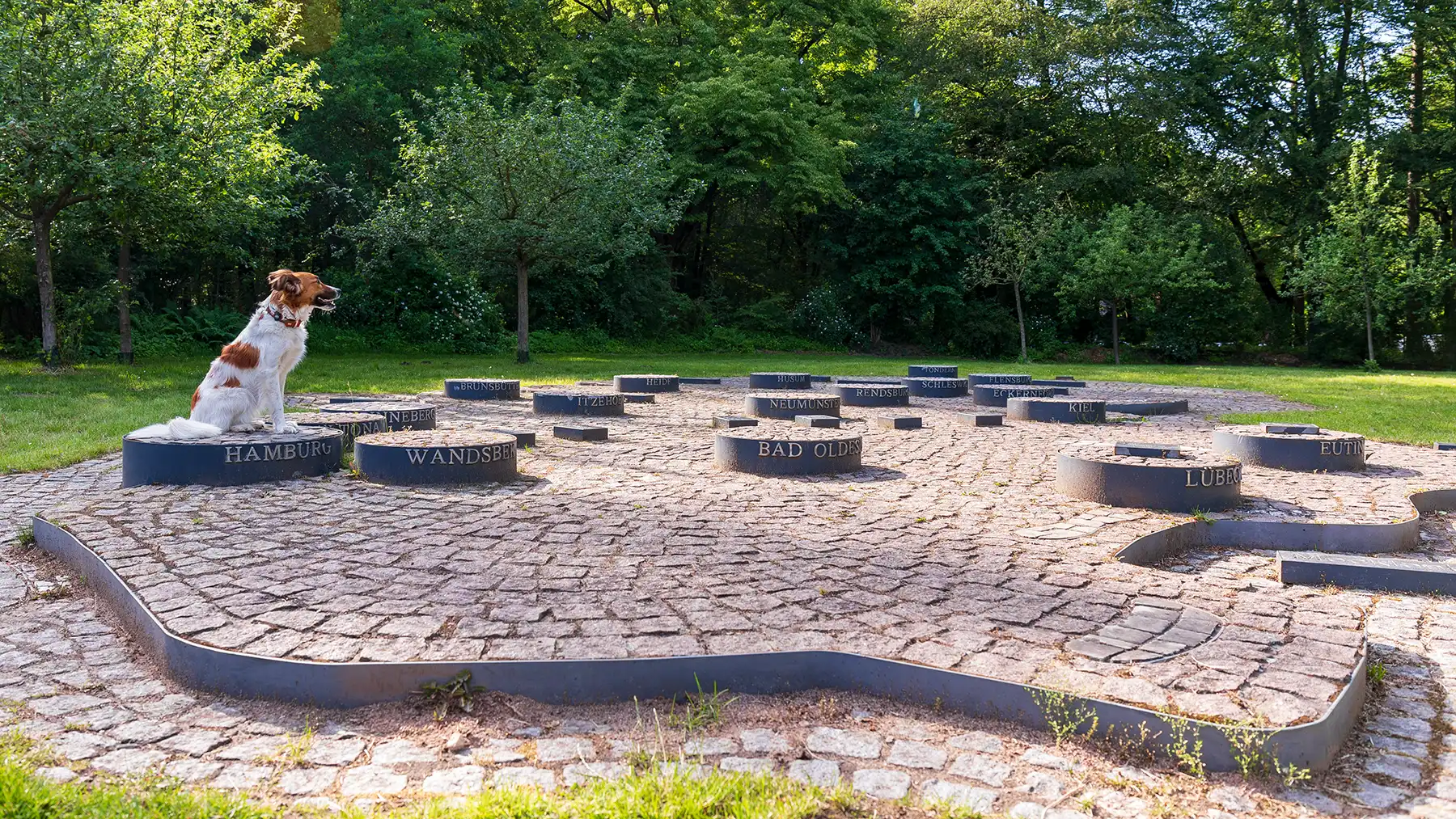 Ein Hund sitzt im Altonaer Volkspark auf dem steinernen Modell des Bundeslandes Schleswig-Holstein